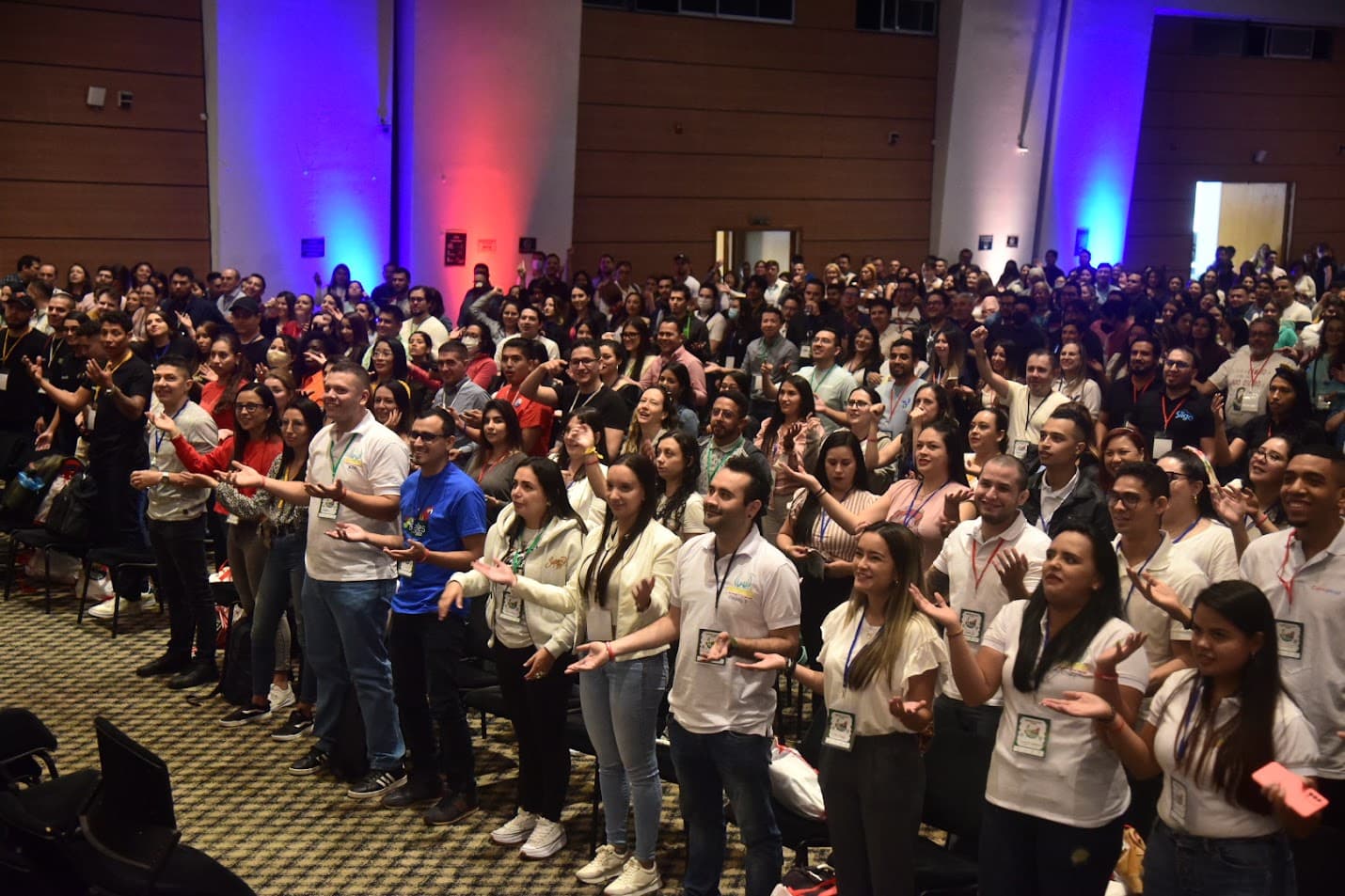 Auditorio lleno de asistentes de pie participando en una actividad
