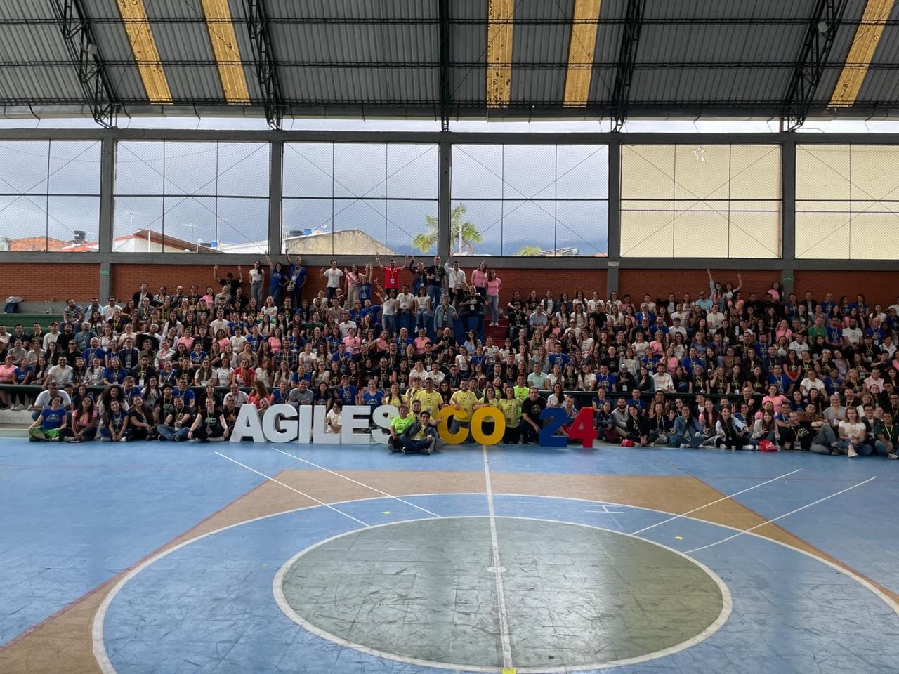 Foto grupal de cientos de asistentes en un coliseo, detrás de las letras de Ágiles Colombia